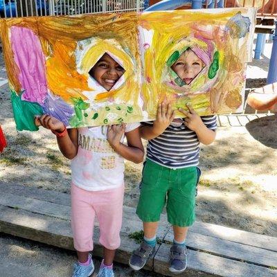 Kids smile through holes in a painted art canvas