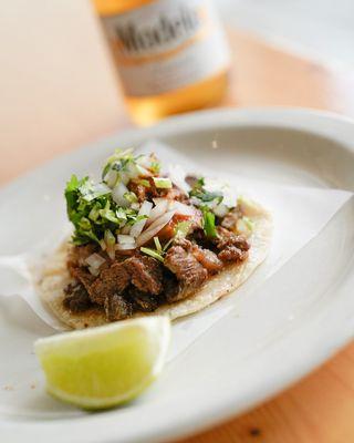 Mouthwatering carne asada taco with a sauce and fresh cilantro and onion