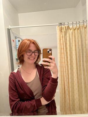 Woman smiles in front of mirror, showing red/orange haircut