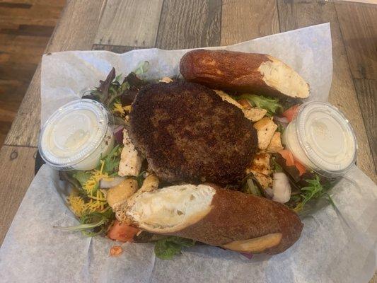 House salad with grilled chicken breast and hamburger patty on top.