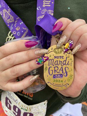 Purple and gold glitter nail color on acrylic nails with nail art gems/charms on each ring finger.