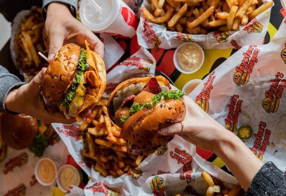 Close up of two people holding their burgers at Taystee's