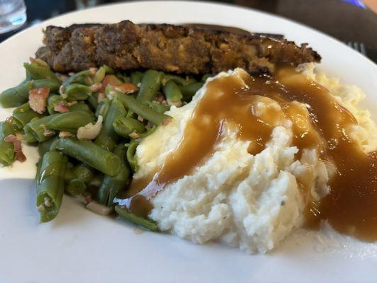 Meatloaf, dinner, green beans with ham, and whipped potatoes with brown gravy.