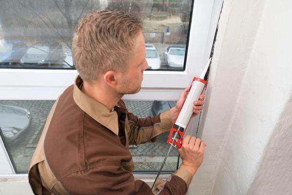 High Angle View Of Young Man In Overall Applying Silicone Sealant