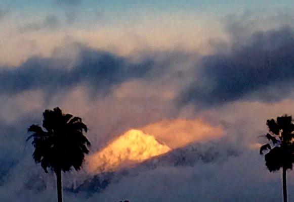 Light from the setting sun reflects off of a snowy mountain peak in stormy skies.