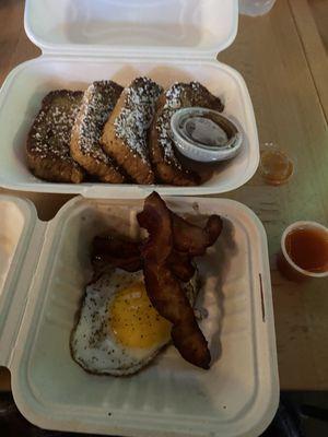 French toast with sides of egg, bacon, and hot sauce