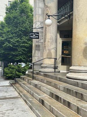 Entrance behind far left column at the top of the stairs