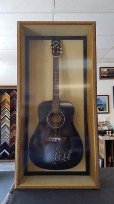 aqustic guitar mounted on gold velvet  and framed in black shadow box frame