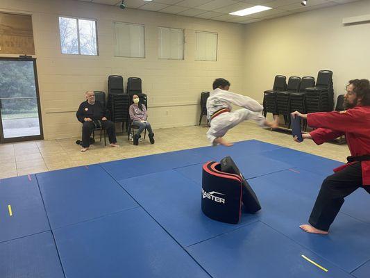 Student performing jumping sidekick board break.