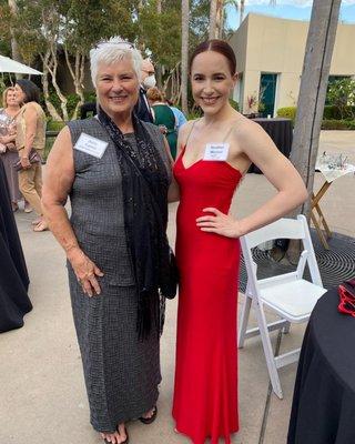 Two white women in formal wear, a gray dress on the left and a red dress on the right, at an awards show.