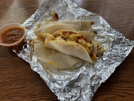 Two breakfast tacos on corn tortillas: eggs, bacon, potatoes, cheese