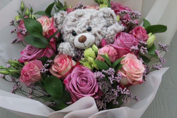 A stunning arrangement of roses, verdant greens, and elegant fillers envelops a beautiful plush nestled within