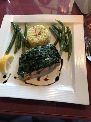 Salmon covered with sautéed spinach served with rice and green beans.