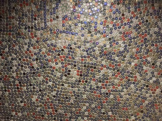 Bunch of bottle caps on bathroom wall