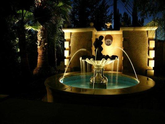 formal Venetian fountain with glass tile and brass nozzle jets and tropical palms.