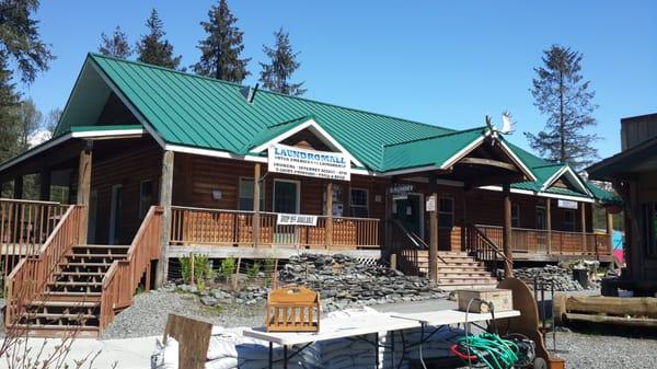 The sunny porch side of the Girdwood Laundromall, right across from the parking, a fruit stand, and a little village park with picnic tables