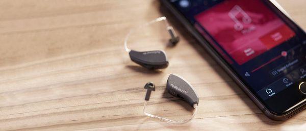 Image of RIC (receiver in the canal) style hearing aids and a Smartphone App that allows the user to make adjustments themselves