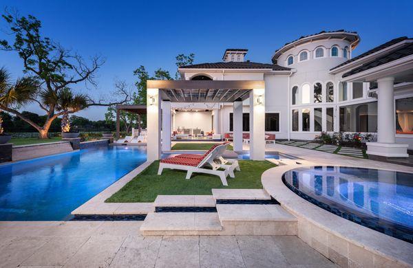 This stunning pool area features a sleek, elongated design surrounded by a luxurious, modern estate. The pool is complemented by a raised sp