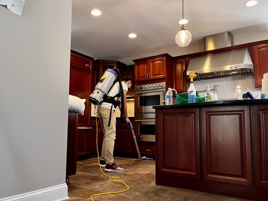 Employee is Vacuuming the kitchen floor.