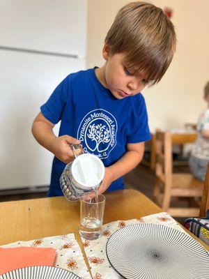 Preschool child pouring water from glass pitcher into a drinking glass in our Montessori classroom.