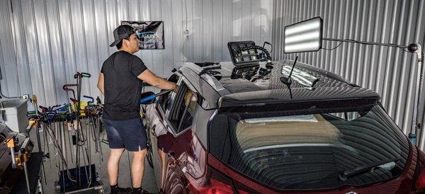 Dent repair tech working on a vehicles roof using metal tools and the lights to fix the dents