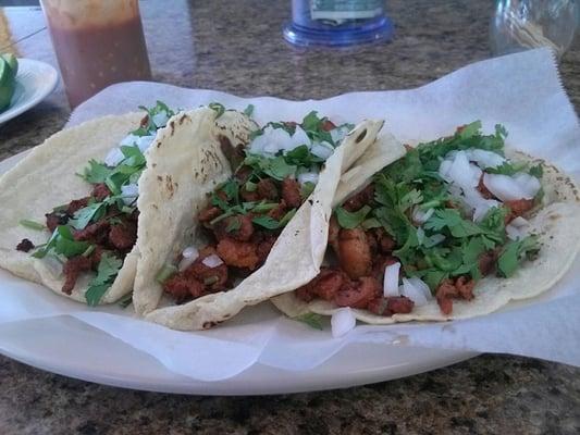 Two tacos al pastor on the left and one taco de pollo on the right.  On fresh made corn tortillas.