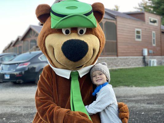 Camper posing with Yogi Bear™ dressed as Boo Boo™ in front of a cabin