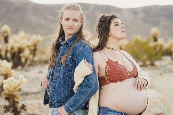 a couple man and pregnant woman in Joshua tree stand effortlessly in the wind. They pose with an essence of rock & roll and boho style