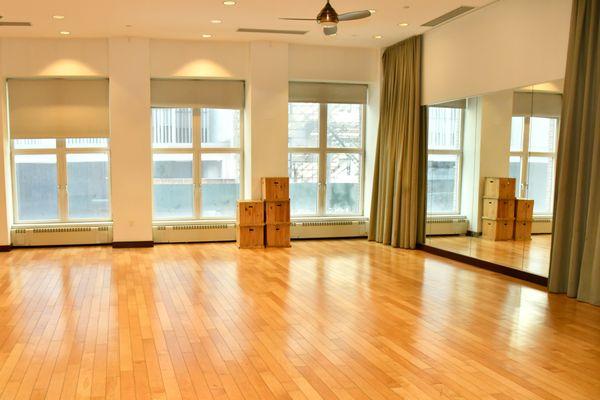 Joseph Jefferson Studio is a beautiful open space with hardwood floors, a wall mirror on one side and natural light from large windows