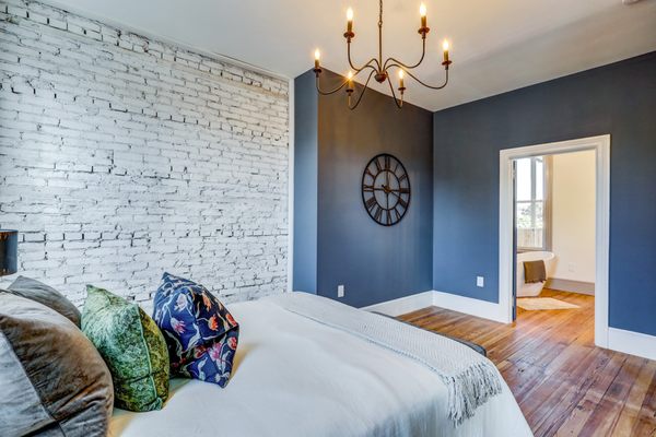 Master bedroom design with whitewashed brick wall, blue accent, black chandelier.