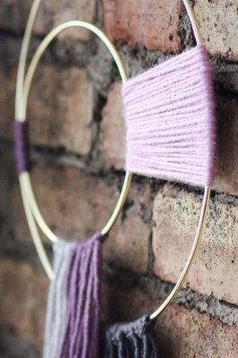 purple and lavender yarn wall art piece hanging on brick wall