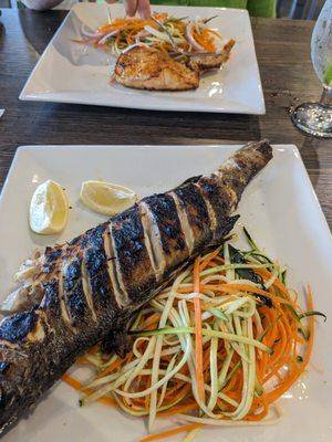 Whole sea bass along with marinated vegetables and salmon in the far background.