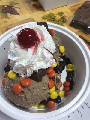 Oreo brownie sundae with chocolate gelato topped with Reese pieces, snickers whip cream and a cherry.