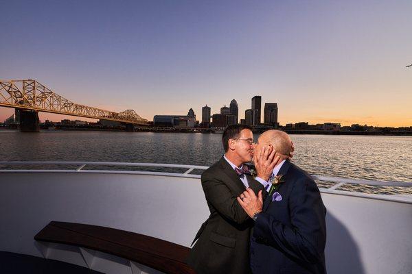 Billy and Joe's wedding portrait kiss aboard the Captain's Quarters yacht, The CQ Princess passing Louisville's skyline.