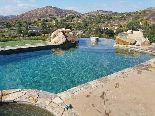 Poway pool cleaning customer with a pebble pool finish and vanishing edge view where we perform weekly pool service