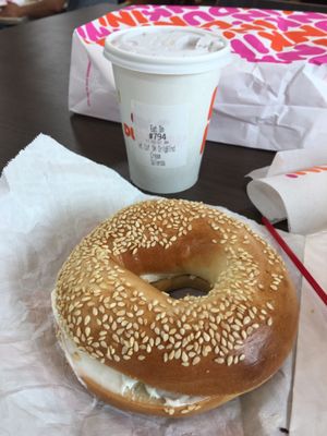 Sesame bagel with cream cheese, small coffee, in the background.