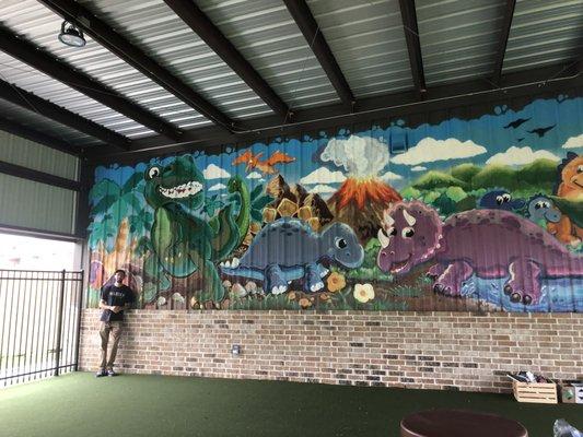 Our Muralist and the Dinosaur wall on the Covered Playground.