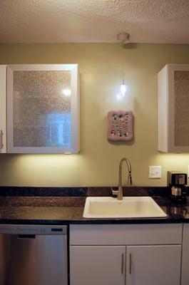 Center view of kitchen with artwork display area and accent lighting fixture. Glass wall cabinet doors by Kraftmaid