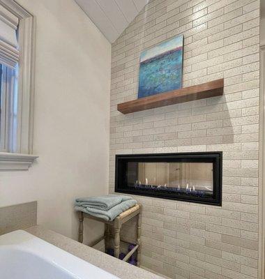 Lovely see-thru fireplace adds to the cozy feel in this neutral, textural primary bathroom. Check out more on Houzz.com