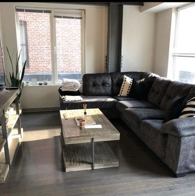 There is a couch , with a table and tv inside this lovely home with big bright daylight windows.