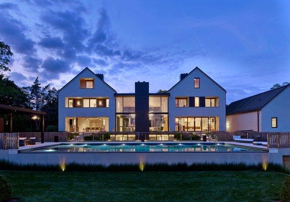 A new modern home designed to serve as an inviting and spacious gathering space, featuring an inground pool captured from the rear view.