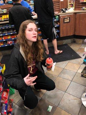 homeless woman holds slushee and poses next to ugly mans feet.