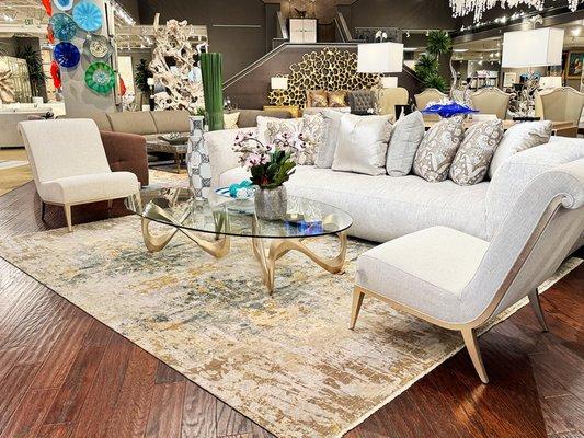 Lavish living room featuring a deep plush sofa, elegant accent chairs, and a glass-top coffee table with a luxurious handmade rug.