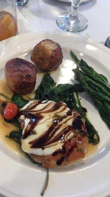 Plated lunch of chicken with cheese and vinaigrette, potatoes, asparagus on a bed of spinach.