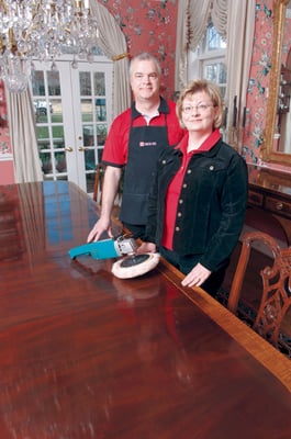 Steve & Corinne Healy next to a dining room table that was just deluxed to a high shine.