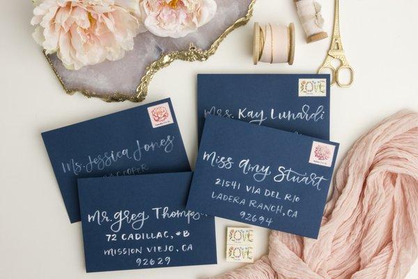 White brush lettering on navy envelopes for a Valentine's Day event