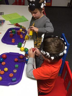 The preschoolers are figuring out math problems with beads on a string.