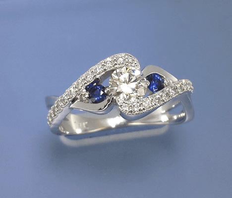 A striking half carat Diamond and top gem Sapphires. The Diamond is held elegantly between the two swirls.  Pave channel Diamonds with milgr