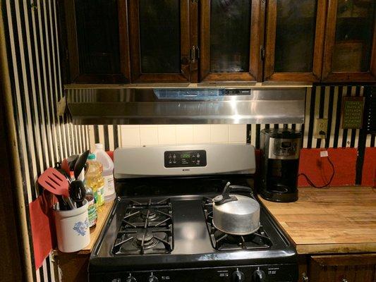 46" silver range hood, beside stove, between coffee maker, on hooks attached to range hood is hanging glass on chain. keeps grease coffee ma