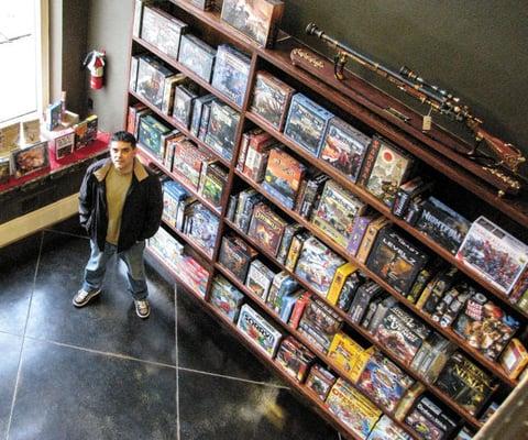 Trent, the owner of Dangerous Gentlemen, or DG, next to his wall of board games for sale.